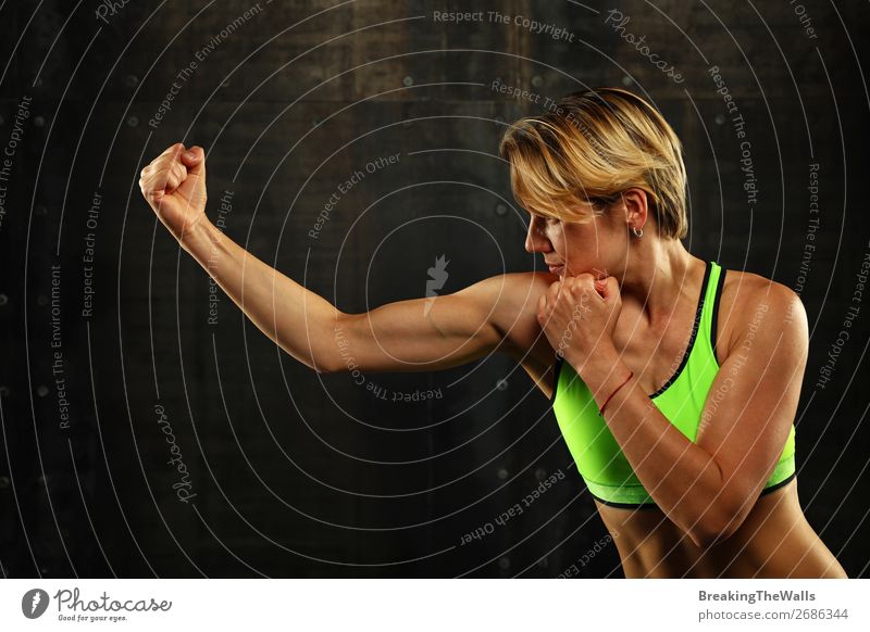 Close up side view profile portrait of one young athletic woman shadow boxing in sportswear in gym over dark background, looking away Sports Martial arts