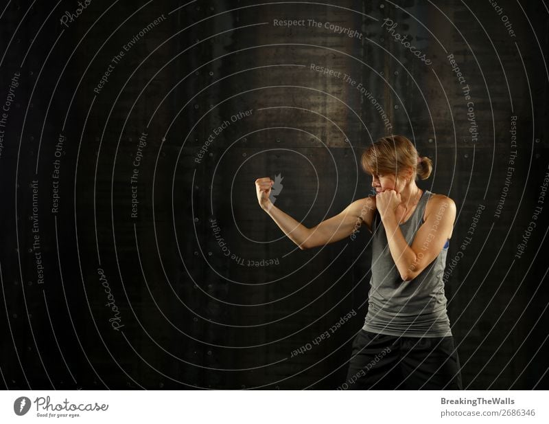 Close up side view profile portrait of one young middle age athletic woman shadow boxing in sportswear in gym over dark background, looking away Lifestyle