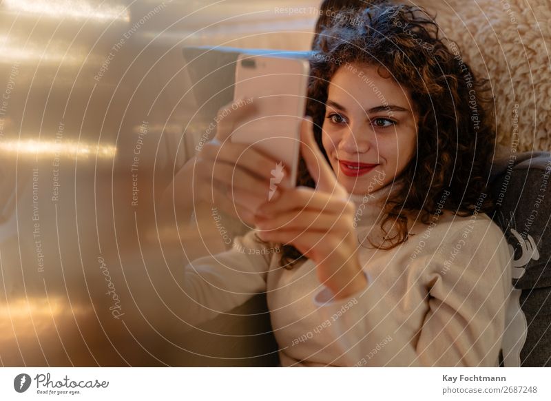 young woman looking at her cellphone Woman attractive beautiful blouse brazilian brown-haired calm caucasian cheerful christmas cozy curly curly hair cute face