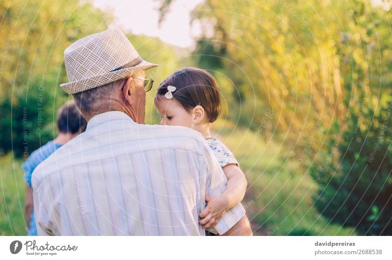 Back view of senior man holding adorable baby girl in his arms over a nature background Lifestyle Happy Relaxation Summer Child Human being Baby Toddler Woman