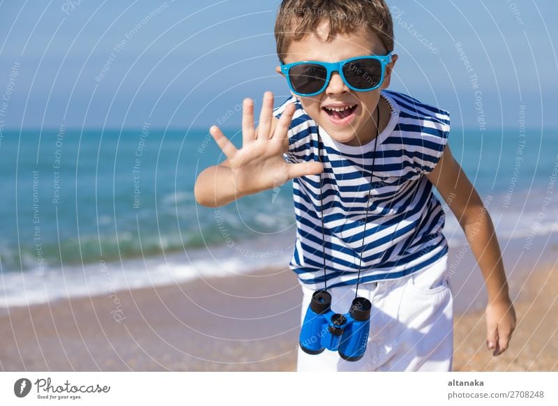 One happy little boy playing on the beach at the day time. He are dressed in sailor's vest. Kid having fun outdoors. Concept of sailor on vacation. Lifestyle