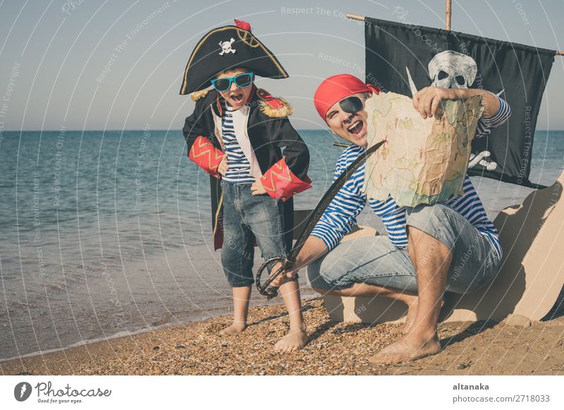 Father and son playing on the beach at the day time. They are dressed in sailor's vests and pirate costumes. Concept of happy game on vacation and friendly family.