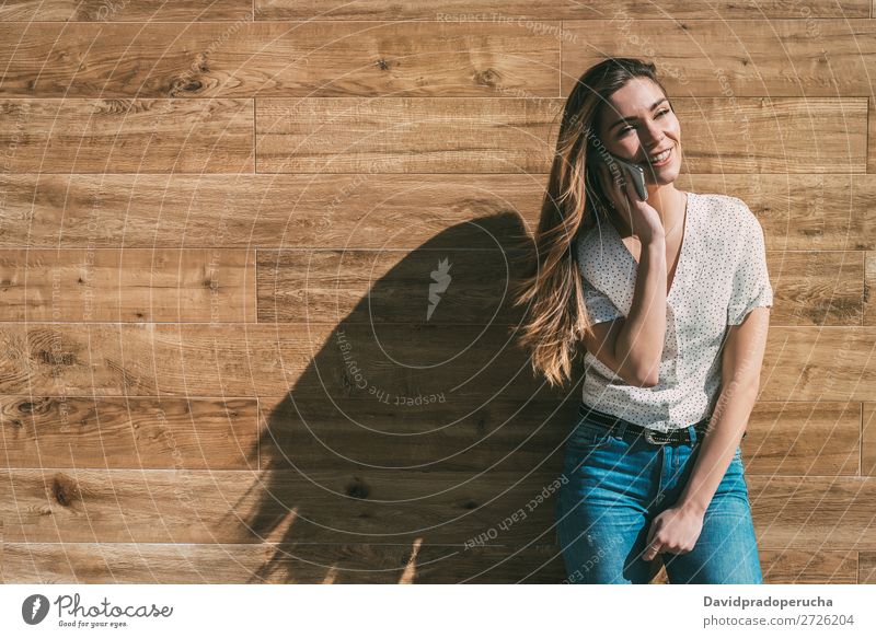 Happy woman using smartphone at a wooden wall Woman PDA Telephone Mobile Communication device Smiling Looking away Portrait photograph Wood Background picture