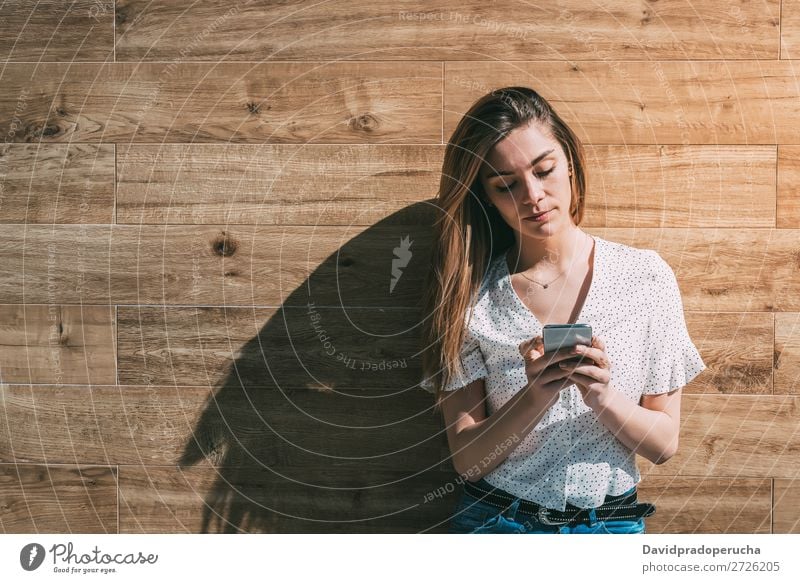 Happy woman using smartphone at a wooden wall Woman PDA Telephone Mobile Communication device Smiling Looking away Portrait photograph Wood Background picture