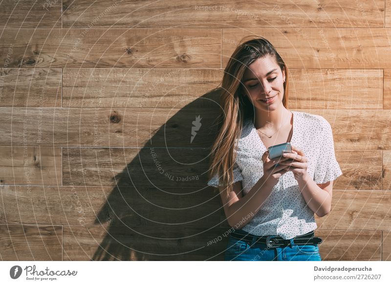 Happy woman using smartphone at a wooden wall Woman PDA Telephone Mobile Communication device Smiling Looking away Portrait photograph Wood Background picture