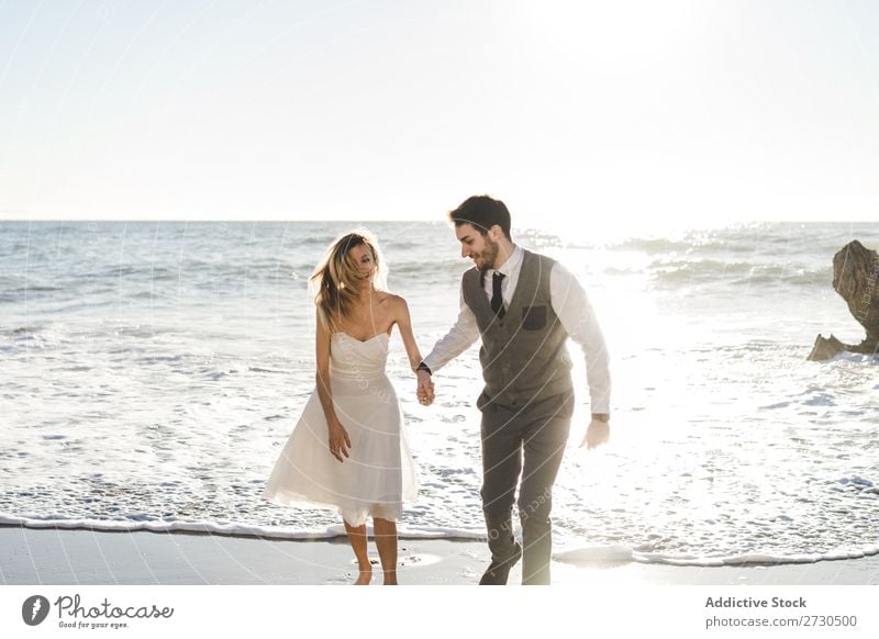 Beautiful bridal couple running on shore Couple Running Beach Happiness seaside holding hands Cheerful Exterior shot Together Contentment Summer Dress Wedding