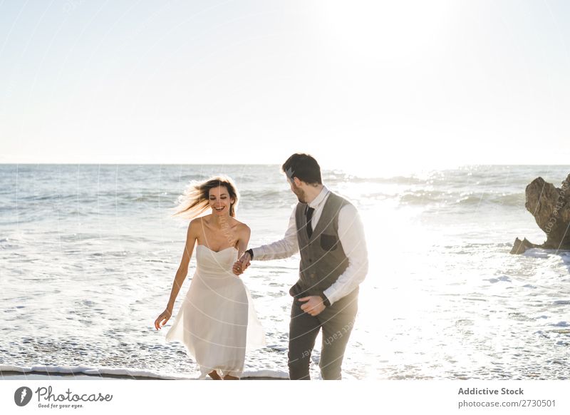 Beautiful bridal couple running on shore Couple Running Beach Happiness seaside holding hands Cheerful Exterior shot Together Contentment Summer Dress Wedding