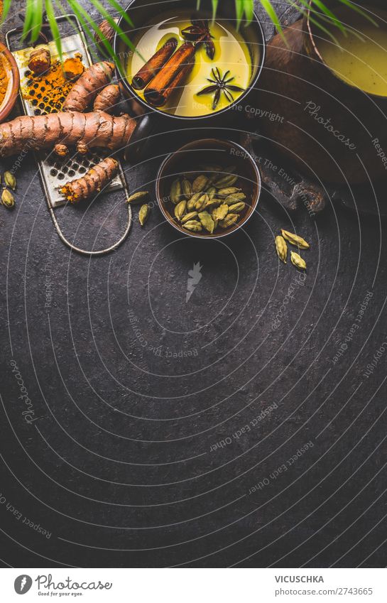 Mug of healthy turmeric milk drink with ingredients: fresh turmeric roots , spices and honey on dark background, top view.  Hot winter beverage. Immune boosting remedy , detox and dieting concept