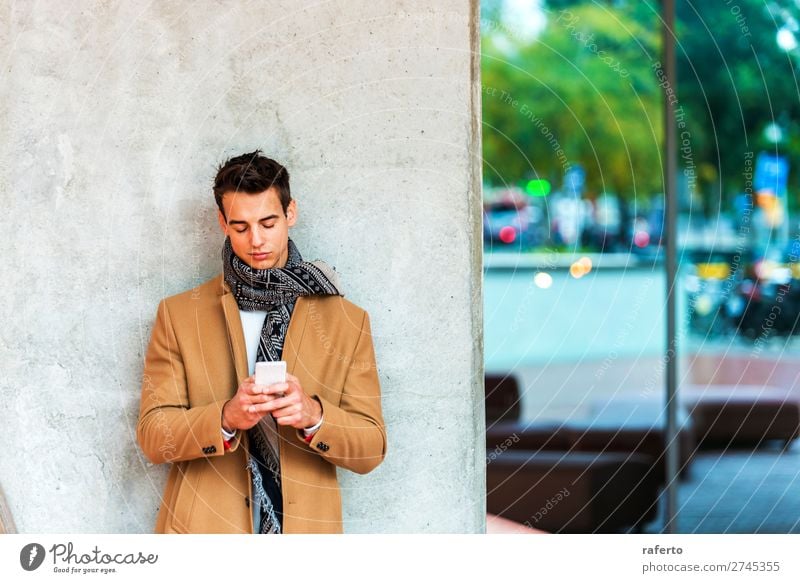 Front view of fashionable young man wearing denim clothes leaning on a wall while using a mobile phone outdoors Lifestyle Elegant Style Beautiful