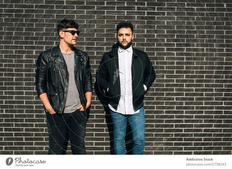 Young homosexual pair looking at camera standing on the background of brick wall. Horizontal outdoors shot. couple gay male love two together lifestyle