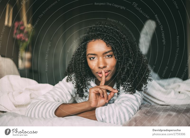 attractive black woman asking for silence with finger on lips on bed Fingers Lips Beautiful Face Mysterious Gesture Woman Bed Portrait photograph Close-up