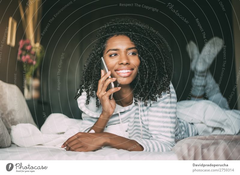 close up of a pretty black woman with curly hair smiling and using phone on bed looking away Woman Bed Portrait photograph Close-up PDA Telephone Mobile