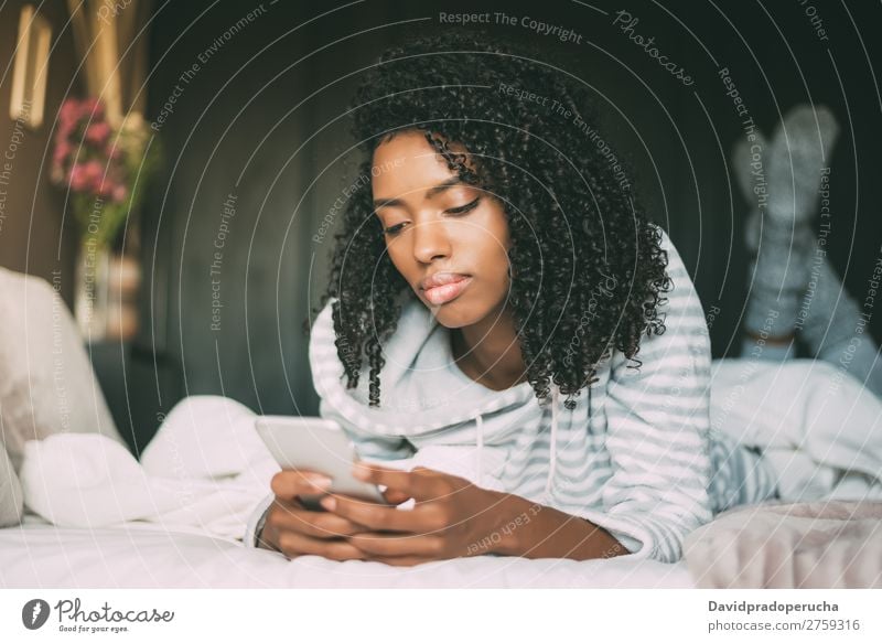 Beautiful serious thoughtful and sad black woman with curly hair using smartphone on bed Woman Bed Mobile Telephone PDA looking down Sadness Anger Black worried