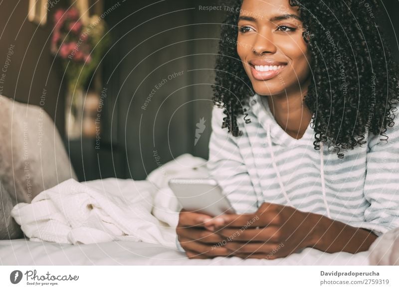 close up of a pretty black woman with curly hair smiling and using phone on bed looking away Woman Bed Portrait photograph Close-up PDA Telephone Mobile