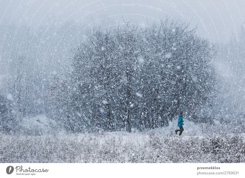 Young man jogging through meadow pathway during heavy snowing. Workout outdoors while winter snow storm Lifestyle Relaxation Leisure and hobbies Winter Snow