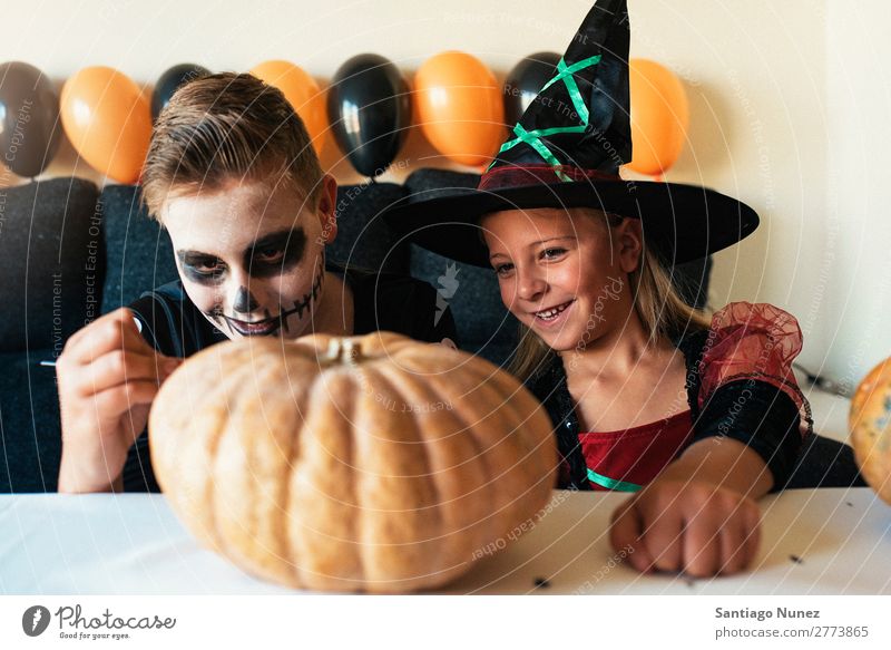 Happy children disguised decorating a pumpkin at home. Hallowe'en Child Girl Boy (child) Painting (action, artwork) Skeleton Witch Disguised Joy