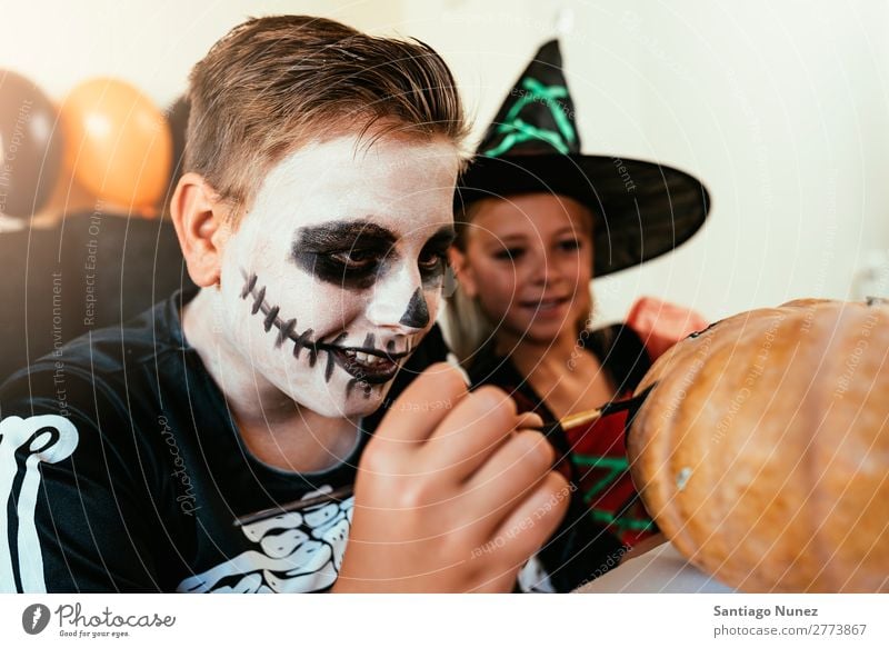 Happy children disguised decorating a pumpkin at home. Hallowe'en Child Girl Boy (child) Painting (action, artwork) Skeleton Witch Disguised Joy