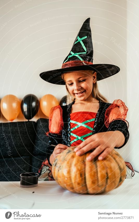 Beautiful girl disguised of witch decorating a pumpkin at home. Hallowe'en Child Girl Painting (action, artwork) Witch Disguised Joy Family & Relations Sister