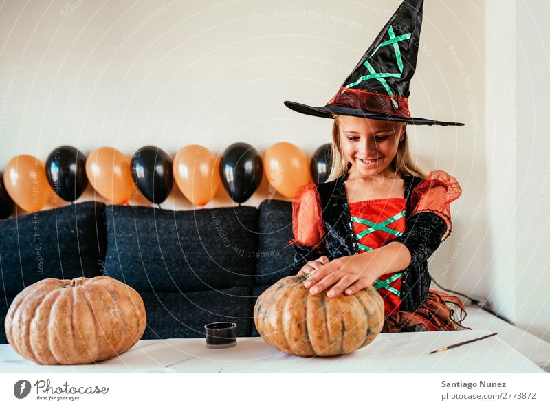 Beautiful girl disguised of witch decorating a pumpkin at home. Hallowe'en Child Girl Painting (action, artwork) Witch Disguised Joy Family & Relations Sister