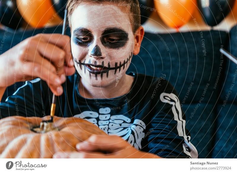 Happy boy disguised decorating a pumpkin at home. Hallowe'en Child Boy (child) Painting (action, artwork) Skeleton Joy Disguised Family & Relations Brother