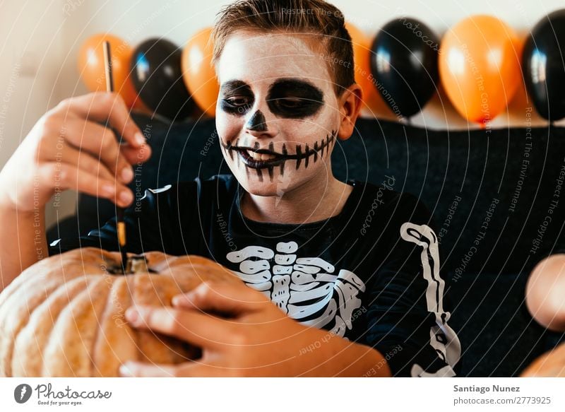 Happy boy disguised decorating a pumpkin at home. Hallowe'en Child Boy (child) Painting (action, artwork) Skeleton Joy Disguised Family & Relations Brother