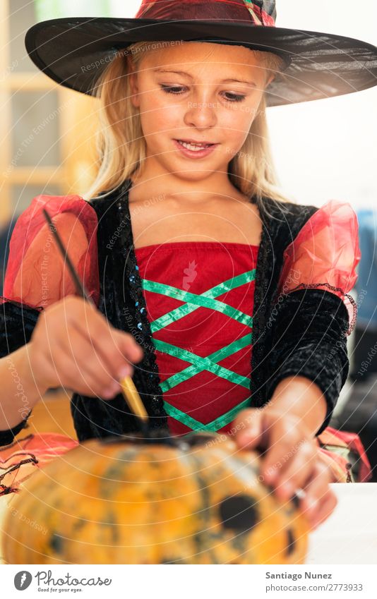 Beautiful girl disguised of witch decorating a pumpkin at home. Hallowe'en Child Girl Painting (action, artwork) Witch Disguised Joy Family & Relations Sister