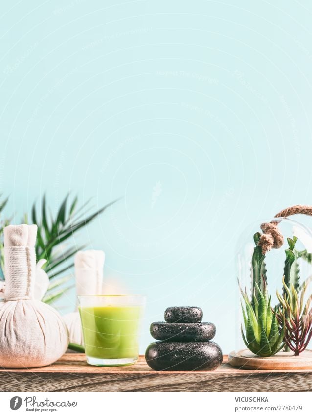 Spa background with massage equipment:  stack of massage stones,  aromatherapy candles,  herbal stamps setting on wooden table with succulent plants at light blue background. Wellness treatment