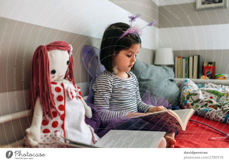 Girl disguised as a butterfly reading with her doll Lifestyle Beautiful Playing Reading Lamp Bedroom Child Human being Woman Adults Friendship Infancy Book