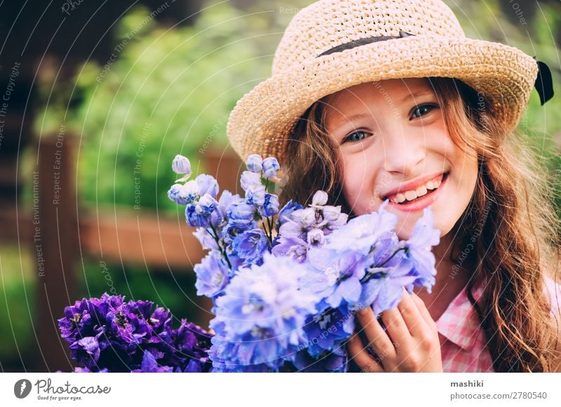 romantic portrait of happy child girl picking bouquet of beautiful blue delphinium flowers from summer garden plant blossom kid play smile funny gardener helper