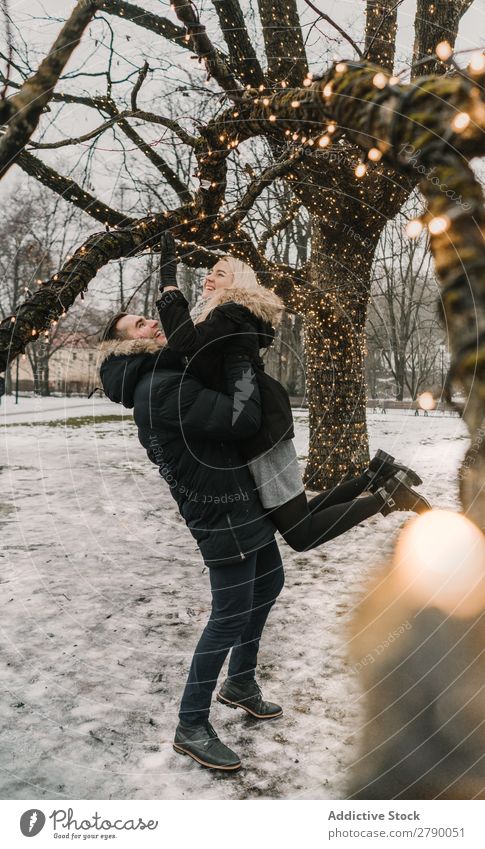 Smiling couple having fun on street near tree with fairy lights Couple Fairy lights Christmas & Advent Street Tree Guy Lady ski jacket Happy Hand Wood