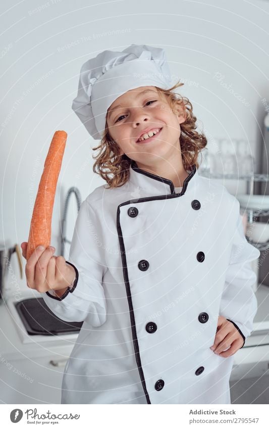 Boy in cook hat with carrot in kitchen Cook Boy (child) Kitchen Carrot chef Child Vegetable Hat Fresh Indicate Hand Hip Cooking Modern Funny Home Light