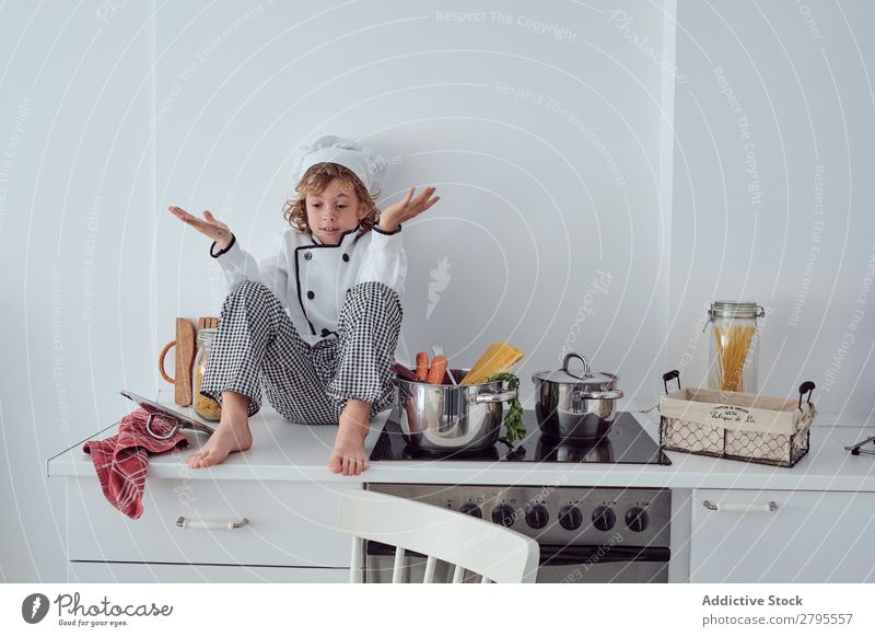 Boy in cook hat sitting near pots on electric fryer in kitchen Cook Boy (child) Pot Kitchen chef Child Vegetable Hat Stove & Oven Cooking Modern Funny Home