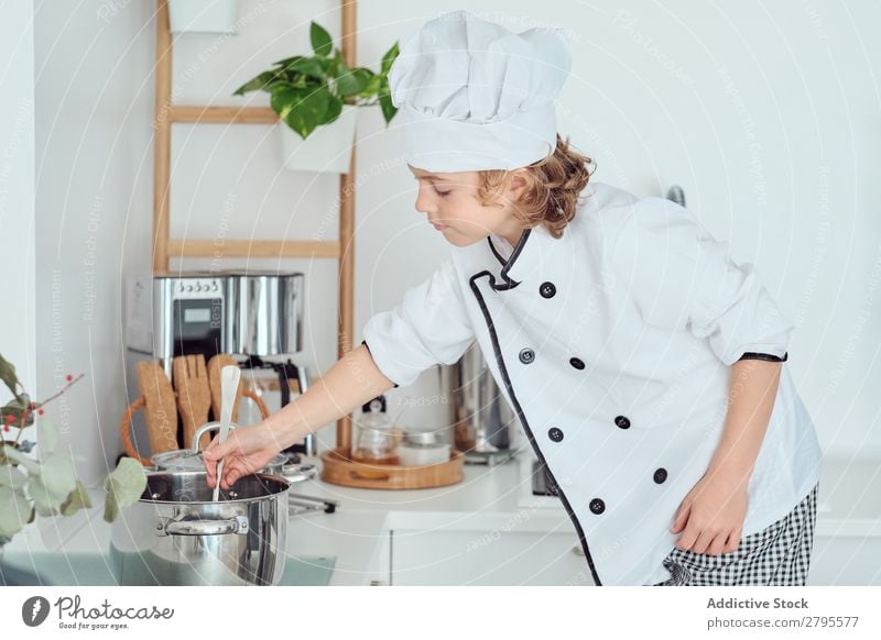 Boy in cook hat with upped hand near pot on chair in kitchen Cook Boy (child) Pot Hand Kitchen Chair chef Child Vegetable Hat Cooking Modern Funny Home Light