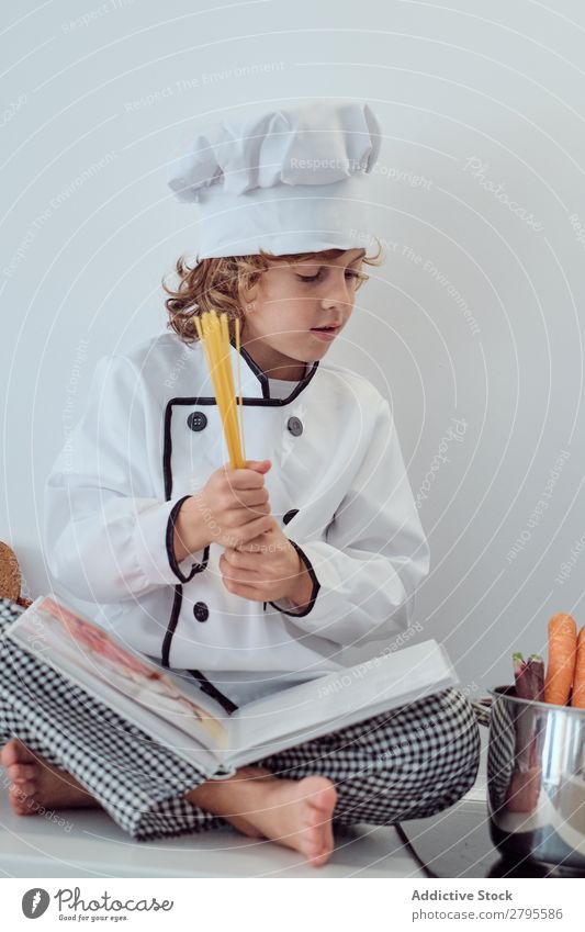 Boy in cook hat putting pasta in pot on electric fryer in kitchen Cook Boy (child) Pot Pasta Kitchen chef Child Macaroni Carrot Vegetable Hat Stove & Oven Putt