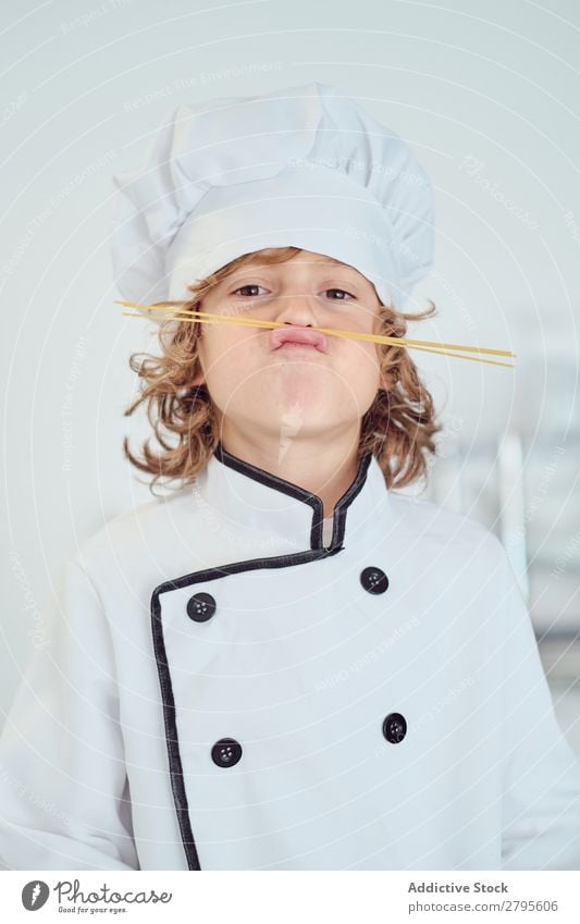 Boy in cook hat making moustache of macaroni in kitchen Cook Boy (child) Kitchen Moustache Macaroni chef Child Hat Pasta Dry Make Cooking Modern Funny Home