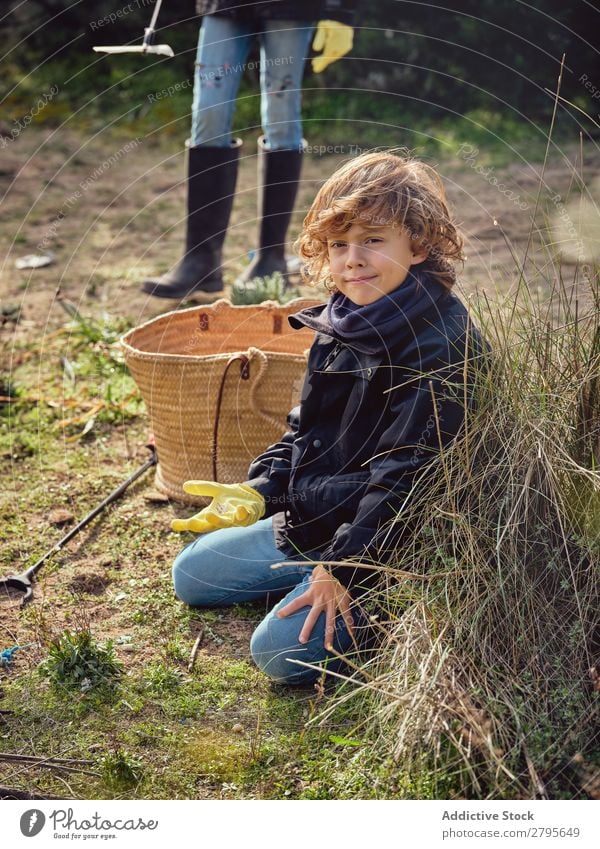 Boy with heap of garbage in hands near basket Trash container picking up Ground Child Park litter picker Boy (child) Container cleaning up Environment Plastic