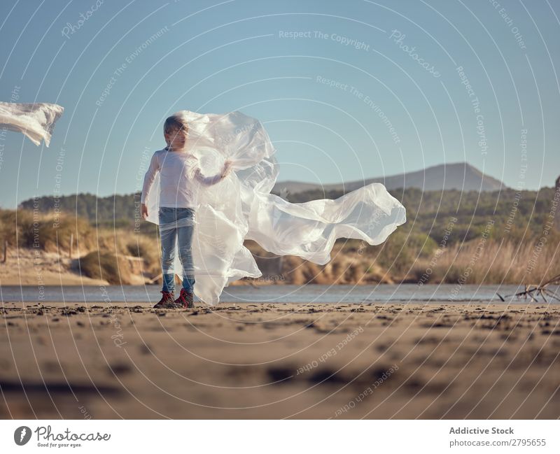 Girl entangled in plastic on river coast Plastic textile waving River Coast Side Wind Sand Water Mountain Landscape Beach Help White Sun Woman Joy Happiness