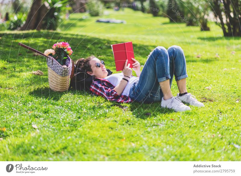 Side view of a hipster happy woman lying on grass in sunny day at park while reading a red book Profile Young woman Hipster Hip & trendy Lie (Untruth) Reading