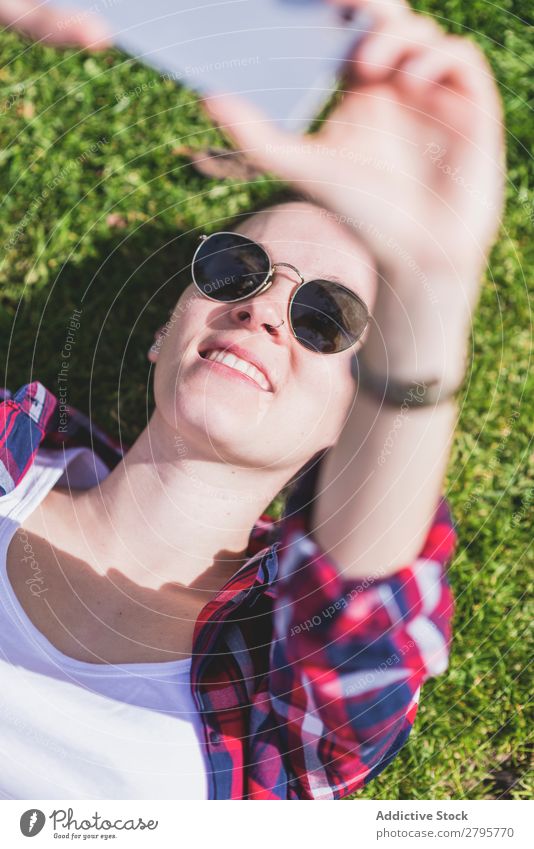 Above view of a young smiling hipster woman lying on grass in a sunny day at a park while taking a selfie with a mobile phone Young woman Hipster Hip & trendy