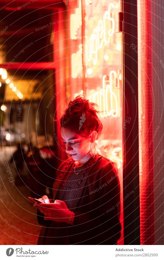 Attractive stylish lady using smartphone near neon lights Woman Style PDA Hip & trendy Neon Tel Aviv Israel Cellphone Hipster Street earrings Light Illumination