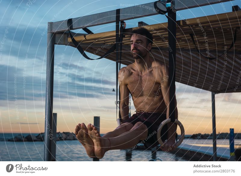 Athletic man balancing on gymnastic rings Man sportsman Balance Embankment Ring shirtless Water City Evening Youth (Young adults) upped legs Sports Action