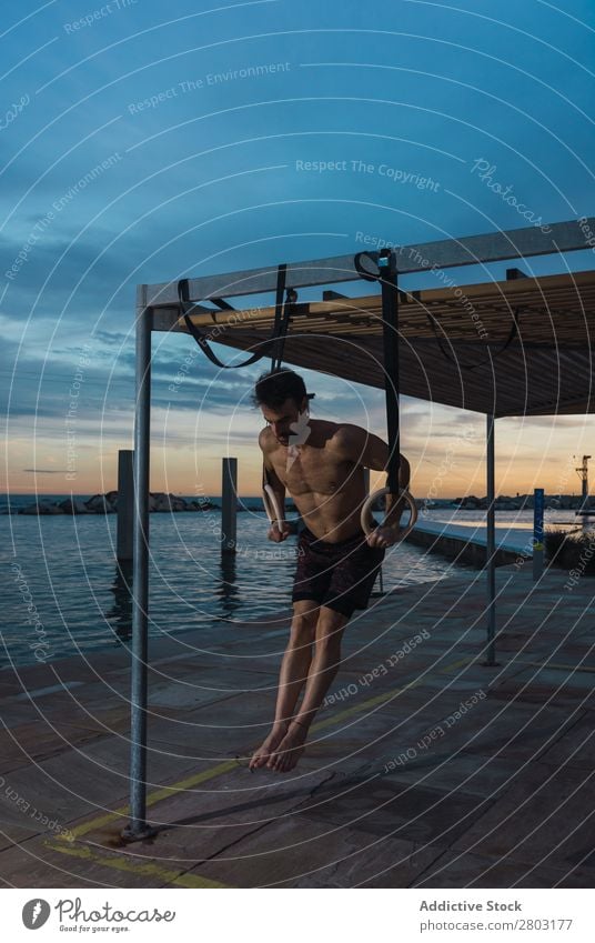 Athletic man balancing on gymnastic rings Man sportsman Balance Embankment Ring shirtless Water City Evening Youth (Young adults) Sports Action workout