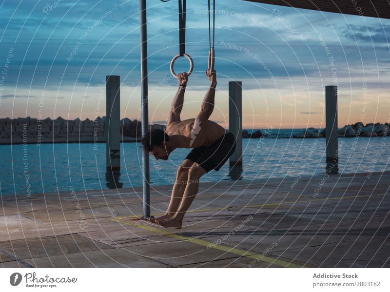 Athletic man balancing on gymnastic rings Man sportsman Balance Embankment Ring shirtless Water City Evening Youth (Young adults) Sports Action workout