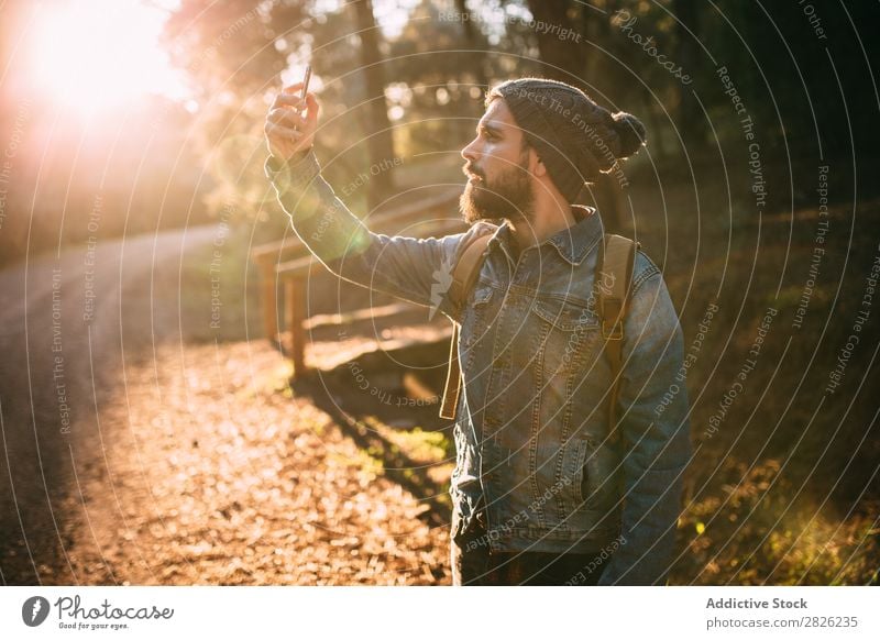 Man taking selfie on sunny autumn road Tourist Forest Portrait photograph Selfie Backpack Telephone Street Technology Autumn Tourism Vacation & Travel Adventure