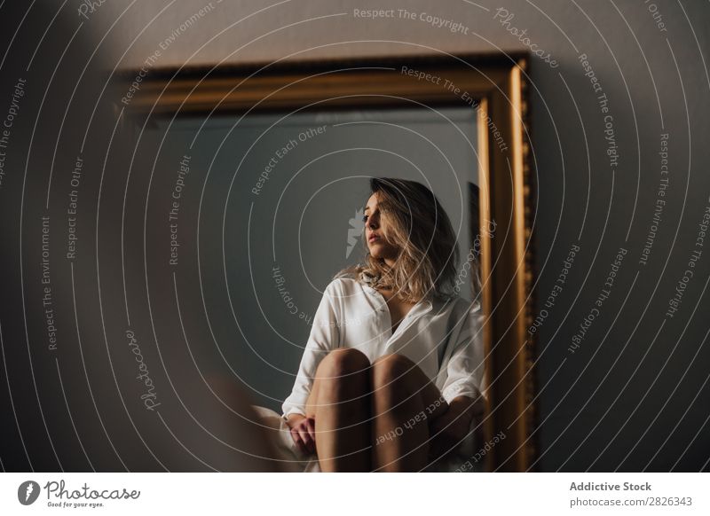 The reflection of female embracing her knees sitting on a bed. Horizontal indoors shot. woman mirror looking away morning home pensive sleepy thoughtful