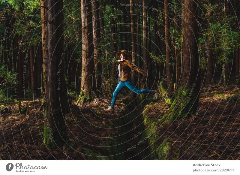 Young woman jumping over drain Woman Tourist Forest Green Nature Environment Jump Water ditch Hat Style pretty Natural Seasons Plant Leaf Light Fresh Bright Day