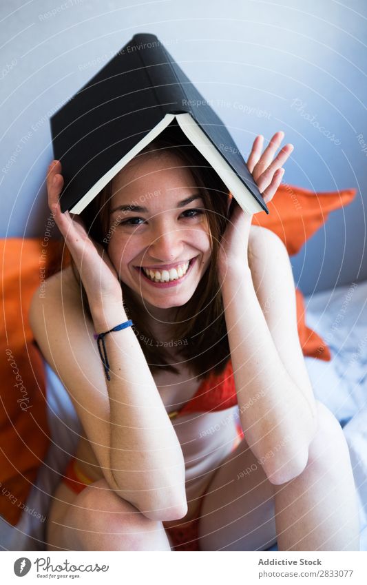 Cheerful girl posing with book Girl Posture Bed Book Creativity on head Joy Underwear Morning Bedroom Laughter Funny Sit Safety (feeling of) Smiling Relaxation