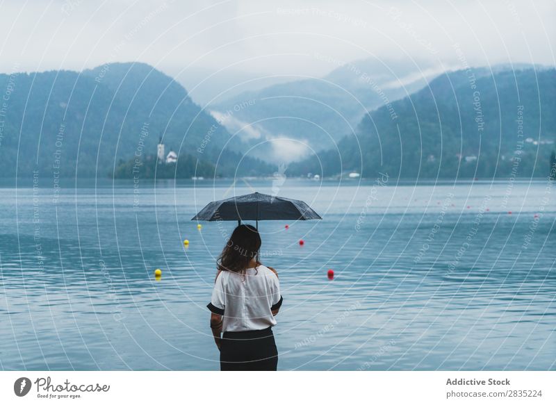 Woman with umbrella on lake Umbrella Lake Stand Mountain Rain Hill Coast Vantage point Nature Water Landscape Summer Blue Green Beautiful Scene