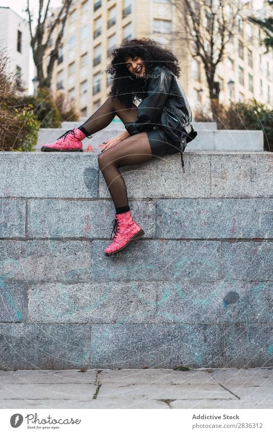 Cheerful woman sitting on wall Woman Attractive City fashionable Curly Brunette Wall (building) Fence Sit Jacket Fashion Youth (Young adults) Beautiful pretty