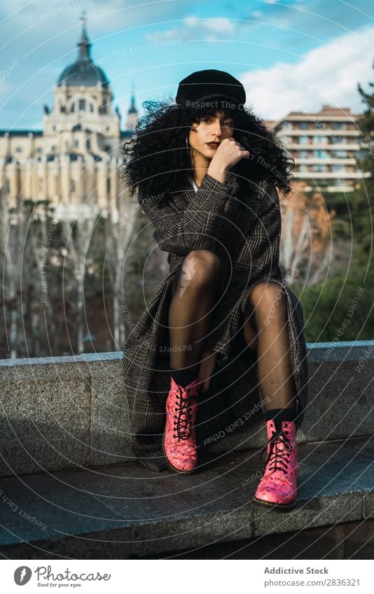 Young stylish woman sitting in city Woman Attractive City fashionable Curly Brunette Coat Hat Sit Fence Vantage point Fashion Youth (Young adults) Beautiful